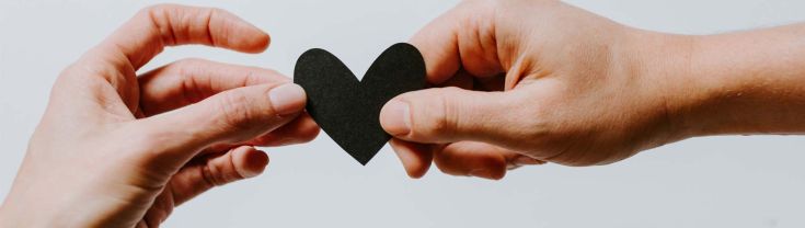 Two hands holding a black paper heart cutout